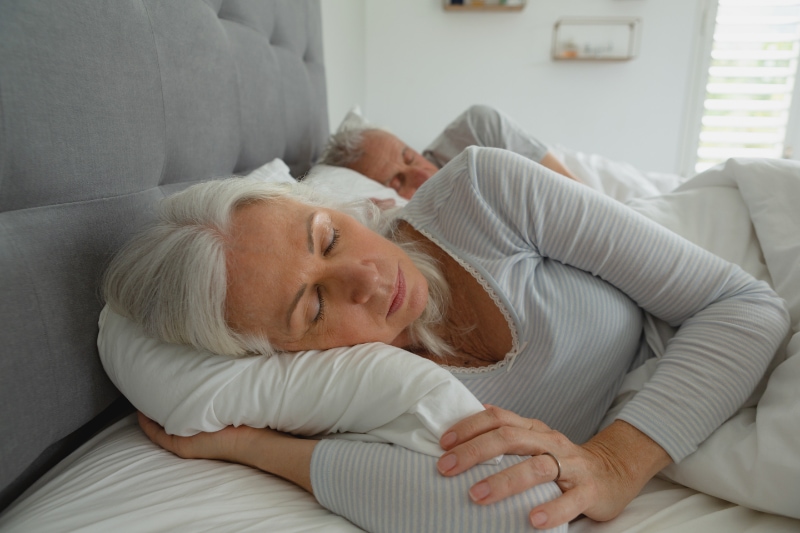 Front view of active senior Caucasian couple sleeping together in bed in bedroom at home.