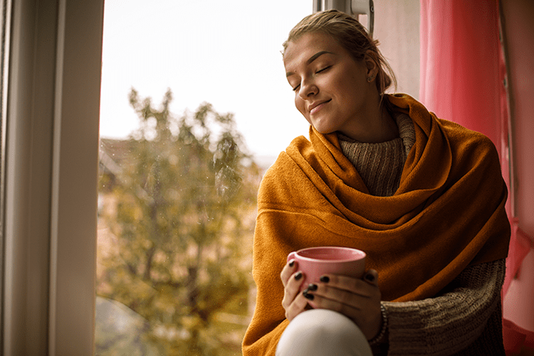 woman sitting by window in fall with coffee