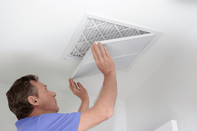 5 Ways to Improve Your Indoor Air Quality. Image shows homeowner checking air filters for dirt.