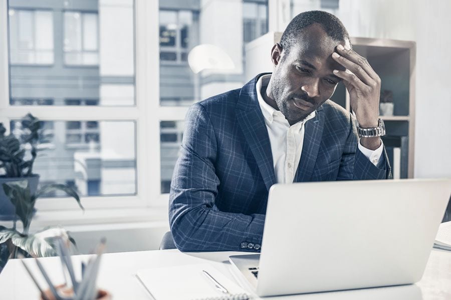 How to Reduce Your Company’s Energy Costs. Image shows man sitting at desk and looking at his laptop.