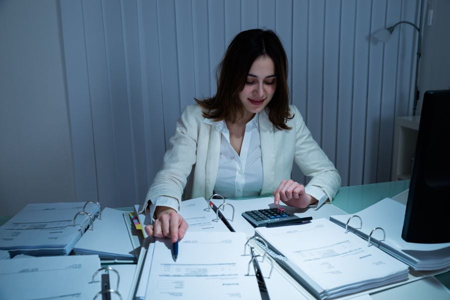 Saving Money on Your Business’s HVAC System. Image is a photograph of a woman with brown hair and a button down shirt sitting at a table and reviewing paperwork.